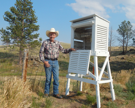 George Portwood standing next to weather station housed in a white wood box that has louvers on sides 