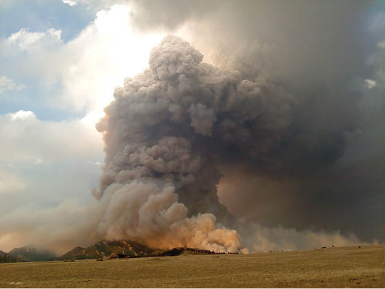 Dramatic shot of billowing smoke towering over mountain peaks  Rangeland in the foreground 