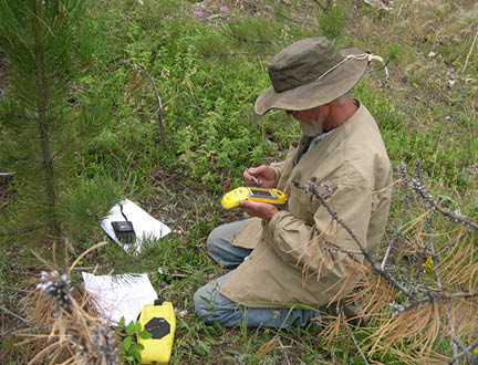 Man kneeling on ground and using a handheld GPS device 